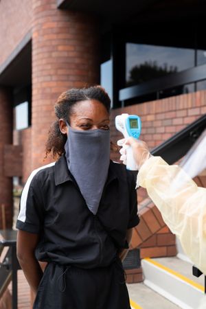 Woman with face mask getting temperature taken before entering building