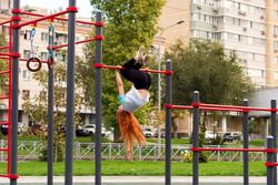 Woman performing gymnastic trick on outdoor horizontal bar in park.