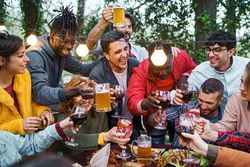 Multi-cultural friends laugh and clink glasses in an outdoor celebration, enjoying a sunny day