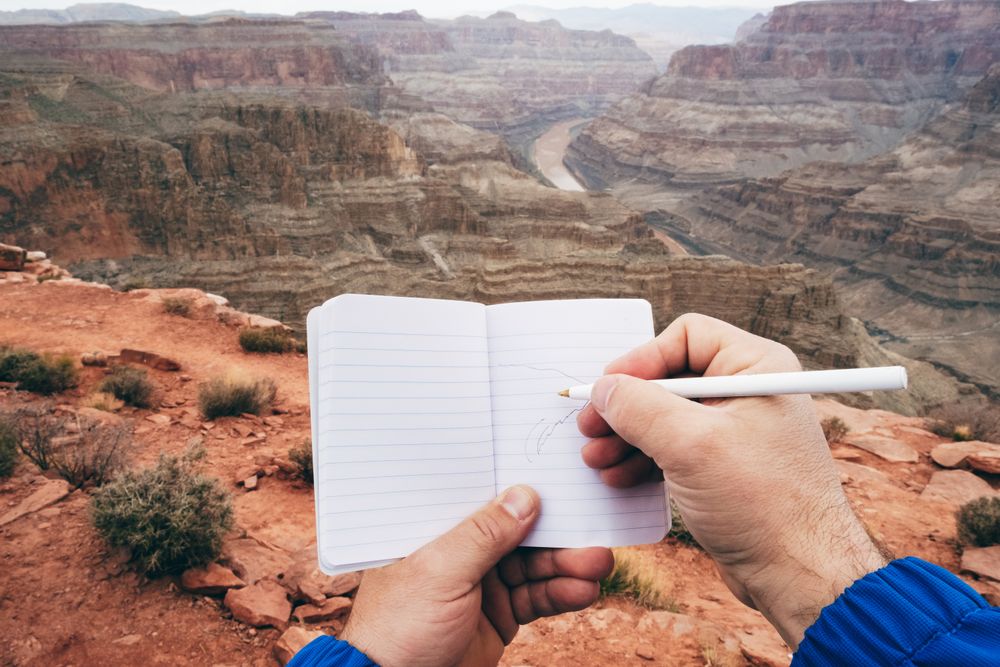 Male drawing in notebook at rock