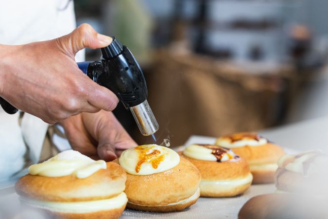 Crop cook burning cream on dessert with gas burner in bakery