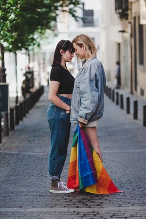 Lesbian couple with LGBT flag standing on street