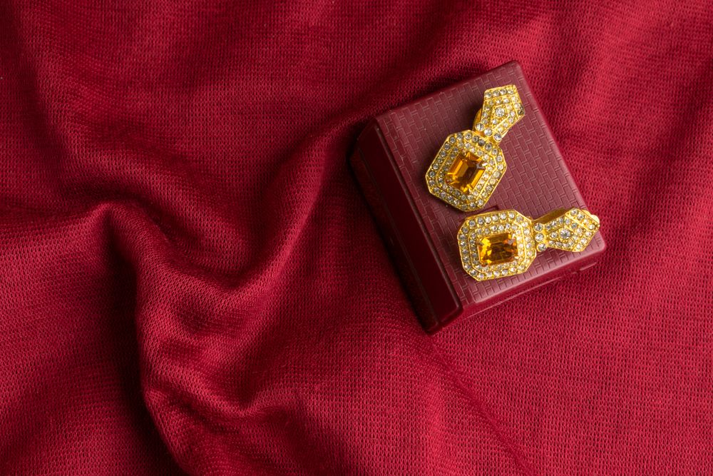 Beautiful shiny golden earrings with diamond studded Indian traditional design on a red velvet background