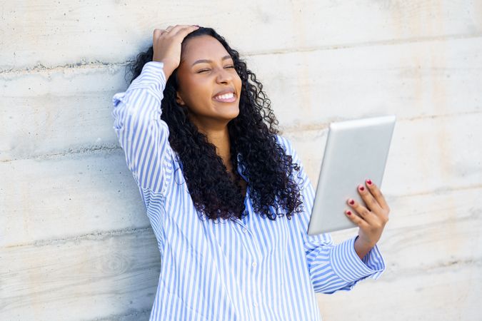 A frustrated woman checks her tablet while leaning against a concrete wall in an urban setting