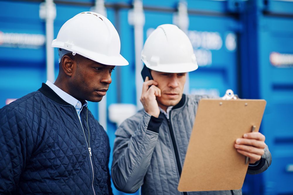 Two serious men in hard hats one on the phone