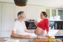 Pregnant woman with glass of water as her husband touches her stomach in kitchen 4jPrr0