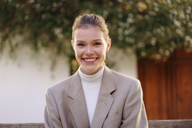 Confident young woman smiling outdoors in stylish blazer, radiating joy and positivity