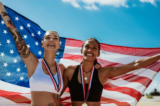 Two woman athletes holding up American flag outdoors
