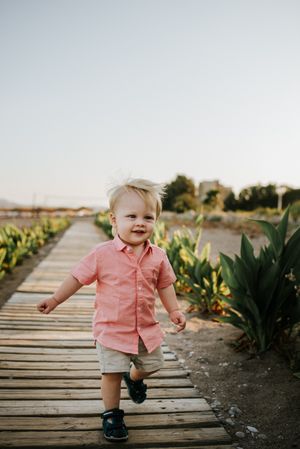 Boy in pink shirt walking in pathway between green field