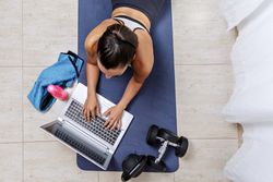 Top view of young woman using laptop sitting beside sport equipment