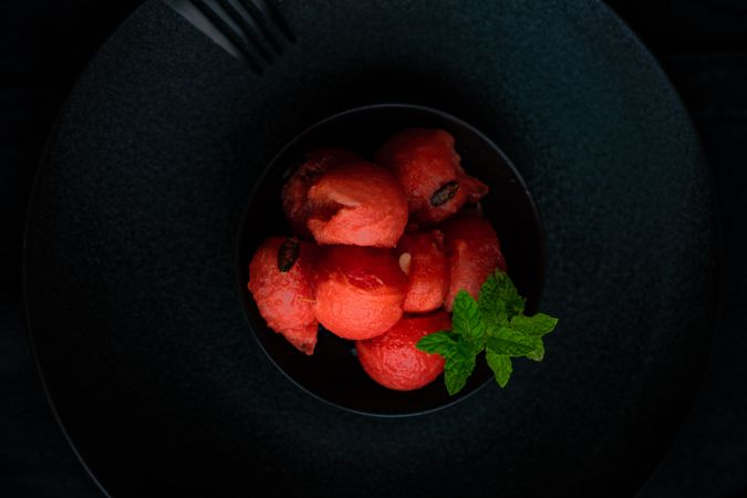 Close up of red sorbet on dark plate, served with mint garnish
