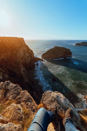 Person sitting on cliff near water