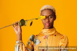 Black woman with short blonde hair holding yellow flower over eye bErNV0