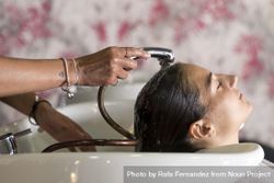 Female with head back in sink at hairdressers with a shower head rinsing her hair 0yZV75