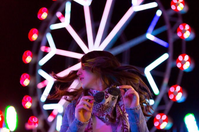 Smiling young woman near illuminated ferris wheel at night