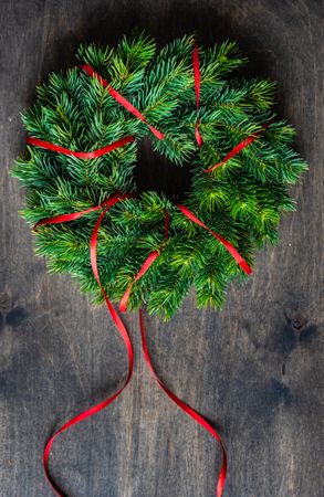 Fir branch wreath with red ribbon on wooden table