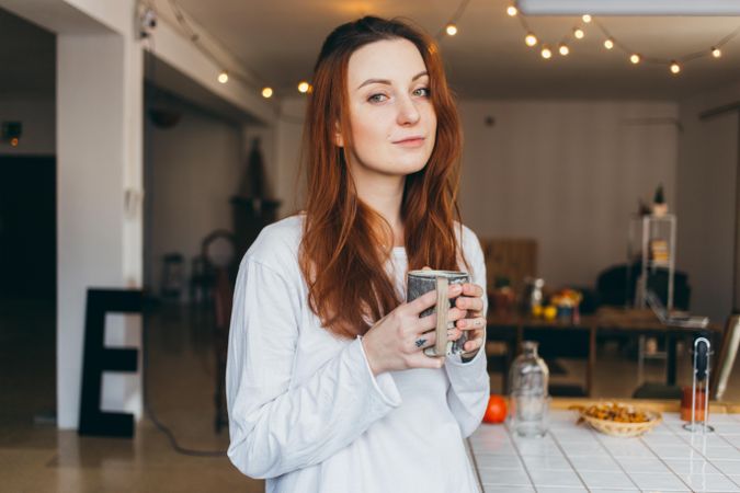Woman looks up while holding mug of a warm drink in her apartment