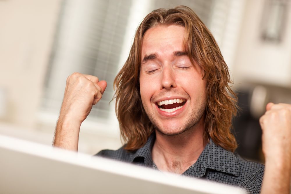 Cheering Young Man Using Laptop Computer