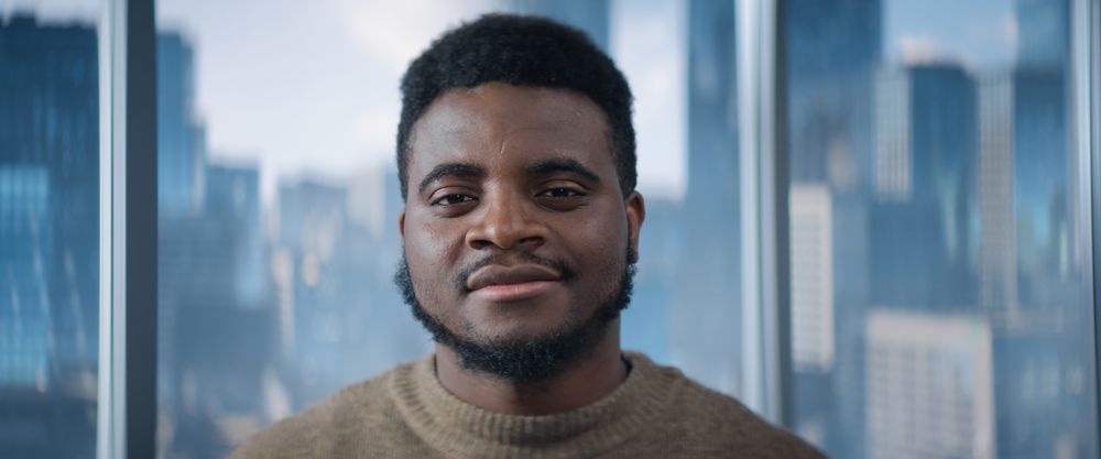 Close Up Portrait of Black Businessman Posing Next to Window in Big City Office with Skyscrapers.