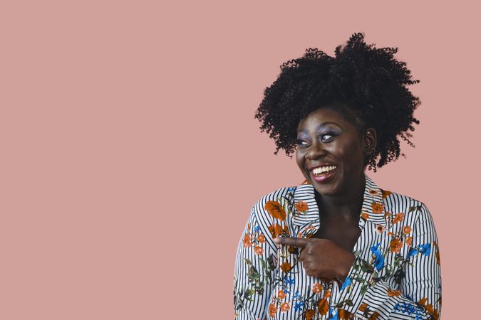 Studio shot of laughing Black woman in floral print shirt pointing at something to the side