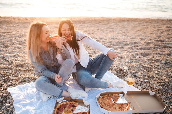 Two women eating pizza on seashore