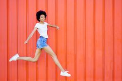 Side view of woman skipping in front of red wall