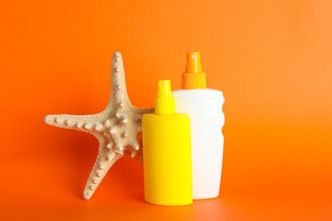 Sunscreen sprays with starfish on color background, space for text