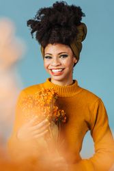 Studio shoot of Black woman holding orange flowers behind orange cloud effect in a blue room