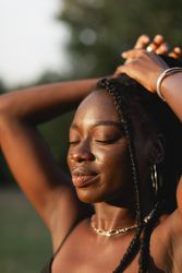A young Black woman with braids, touches her hair, feels beautiful, and enjoys the sun during a sunset stroll