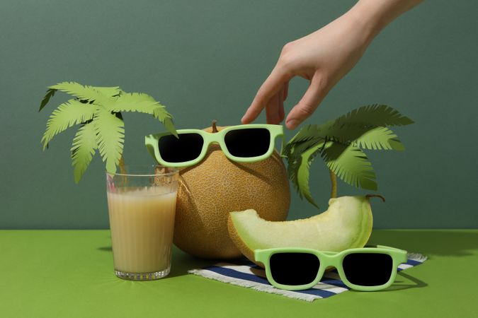 Fresh melon with sunglasses on green background