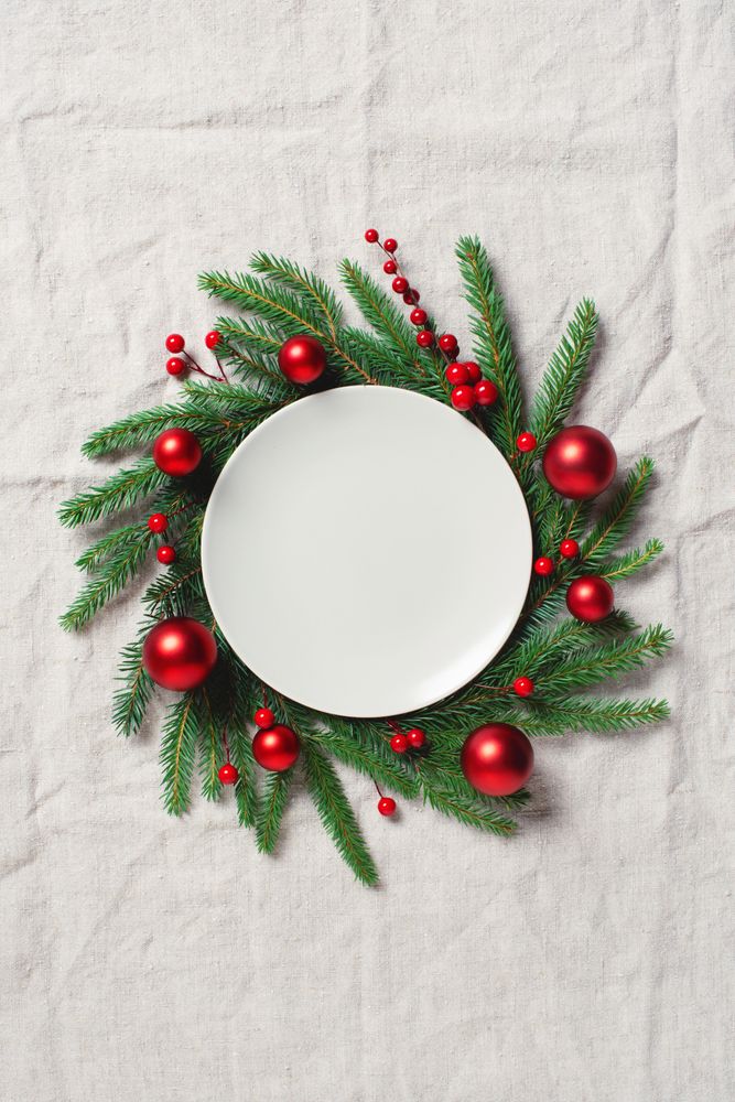Top view of festive place setting of dinner plate with fir wreath and red baubles