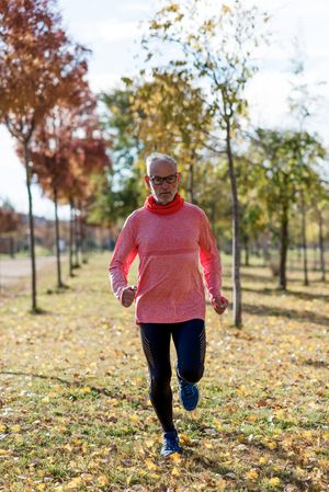 Grey haired male jogging in park with fall leaves