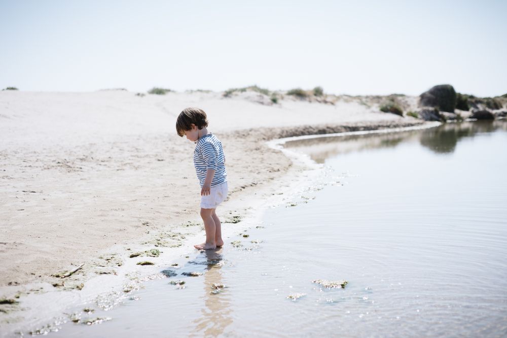 Barefoot child in short watching waves on sandy beach