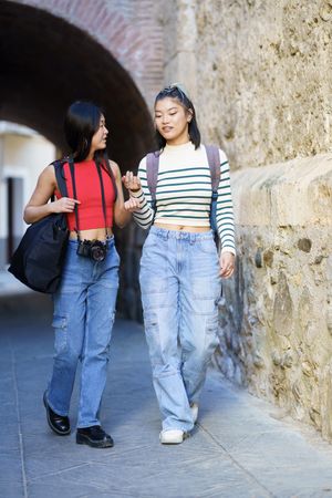 Two women in jeans walking outside in town with bags and camera