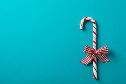 Sweet candy cane with bow on turquoise background, space for text