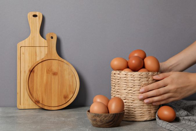 Eggs in a wicker basket, with a hand, on a gray background.