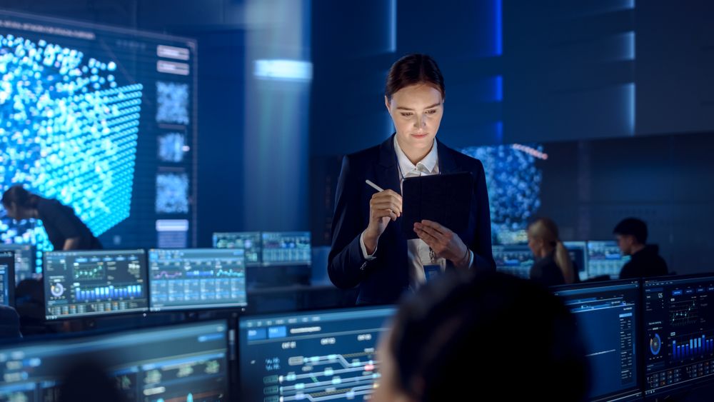 Professional Woman Uses Tablet in High-tech Control Room. Monitors Display Data Analytics.