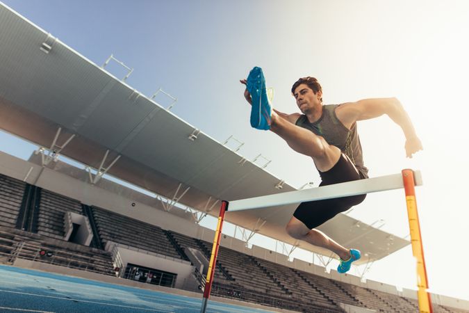 Athlete jumping over an hurdle on running track with empty stands
