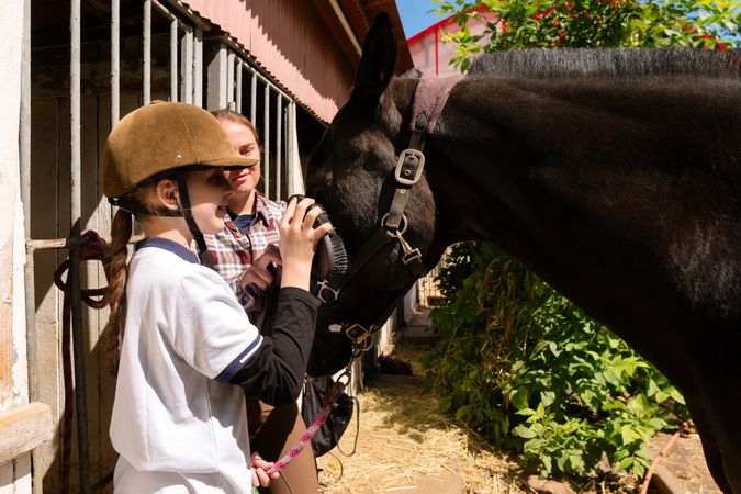Girl brushes horse's nose while instructor looks on.
