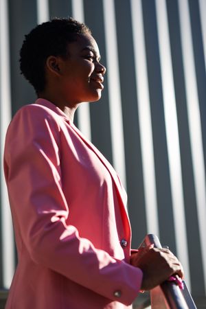 Side view of female wearing suit with pink jacket outside office with striped shadows