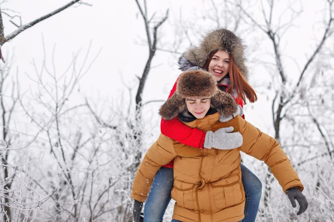 Happy teenage girl on back on boyfriend in snowy forest