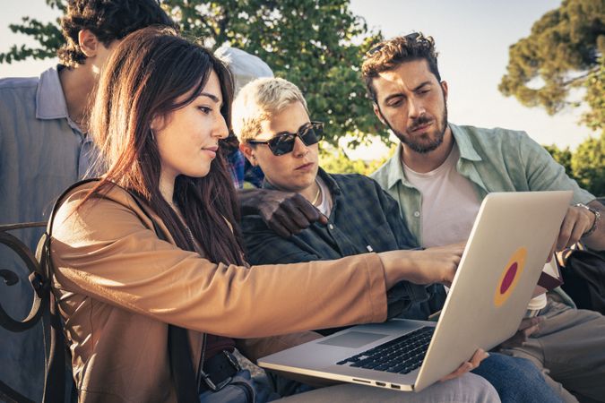 Group of people collaborating outdoors using laptop computer for teamwork project