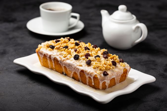 Fruit cake topped with icing, walnuts and raisin, with tea pot