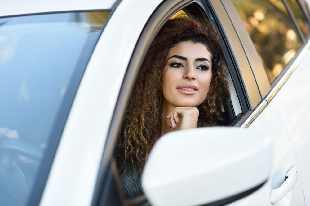 Smiling female with curly hair resting chin on hand out driver’s window
