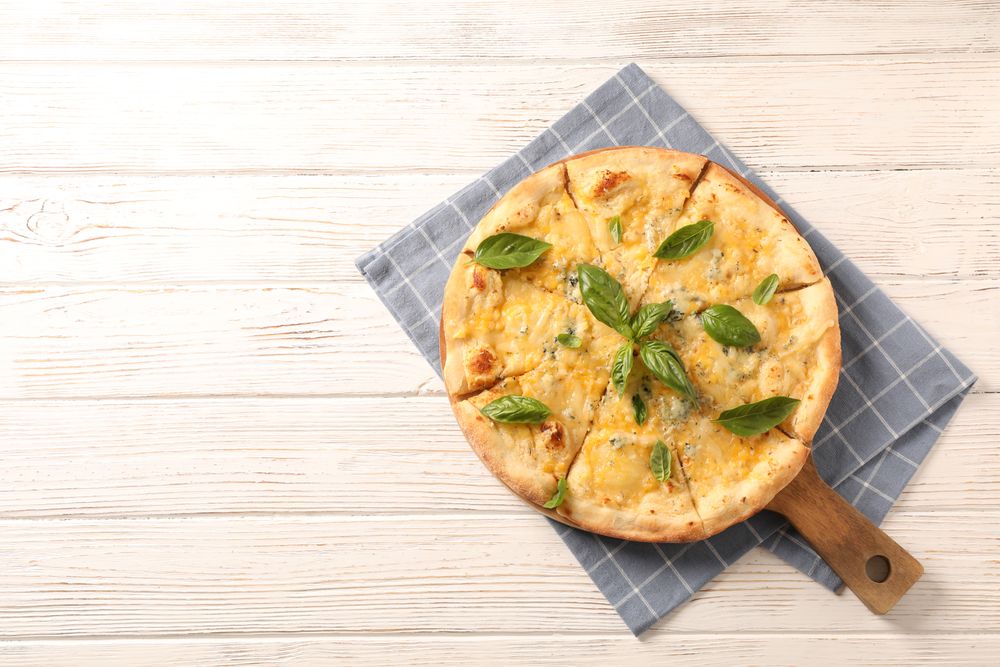 Towel, board, cheese pizza with basil on wooden background, copy space