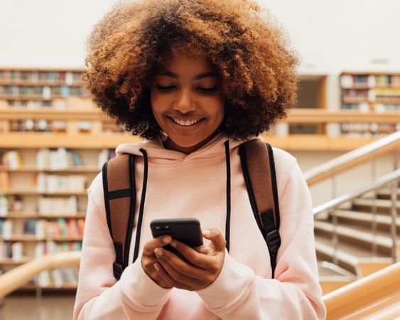 Teenage female student smiling while texting in library