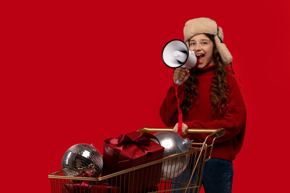 Smiling girl in red sweater and fur hat holds megaphone