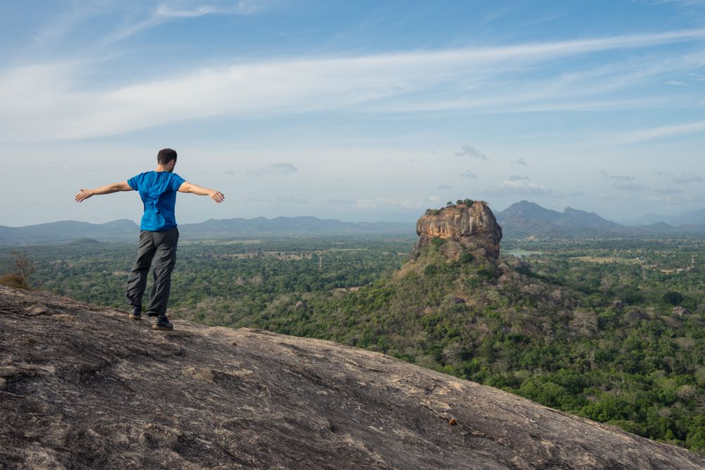 Tourist against solitary rock in middle of green forested plain under clear sky in summer