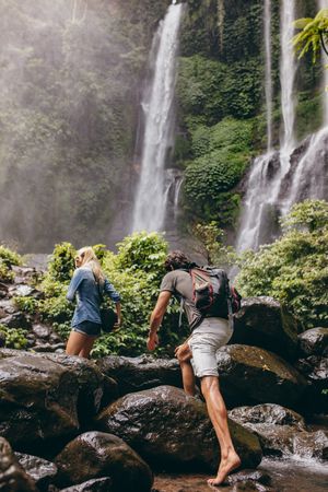 Man and woman climbing up rocks toward a waterfall