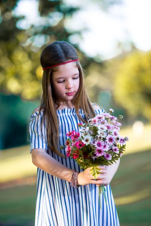 Girl in blue striped dress holding a bouquet of flowers standing outdoor
